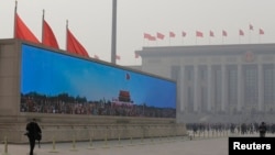 A large screen shows Tiananmen Gate under blue skies at Beijing's Tiananmen Square as delegates arrive for a plenary session of the National People's Congress (NPC) at the Great Hall of the People (R) in the dust storm and haze, Mar. 8, 2013.