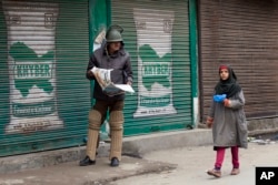 FILE - An Indian policeman reading newspaper watches a Kashmiri girl walk past him during restrictions in Srinagar, Indian controlled Kashmir.