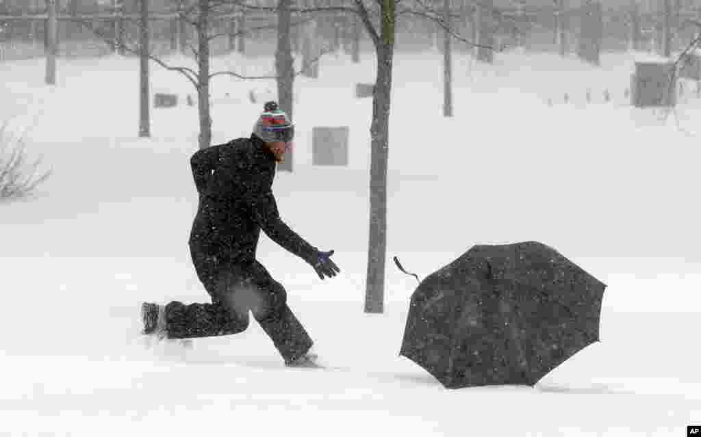 Seorang pria mengejar payungnya yang tertiup angin dalam badai salju di Boston (27/1). (AP/Steven Senne)