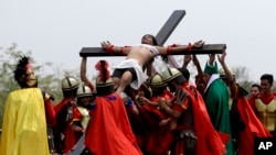 Devotos vestidos como soldados romanos levantan a Ruben Enaje en la cruz después de haber sido clavado por trigésima segunda vez durante la recreación de la crucifixión de Jesucristo en un ritual del Viernes Santo en Filipinas, el viernes, 30 de marzo, de 2018.