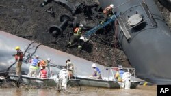 FILE – Workers remove damaged CSX tanker cars carrying crude oil after they derailed and caught fire along the James River near downtown Lynchburg, Virginia, May 1, 2014. 