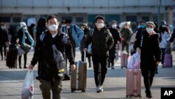 Travelers wear face masks as they walk outside the Beijing Railway Station in Beijing, Saturday, Feb. 15, 2020. (AP Photo/Mark Schiefelbein)