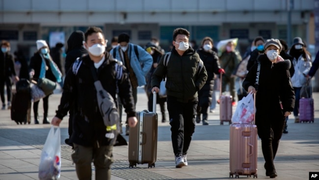 Travelers wear face masks as they walk outside the Beijing Railway Station in Beijing, Saturday, Feb. 15, 2020. (AP Photo/Mark Schiefelbein)