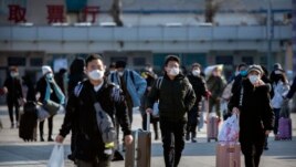 Travelers wear face masks as they walk outside the Beijing Railway Station in Beijing, Saturday, Feb. 15, 2020. (AP Photo/Mark Schiefelbein)