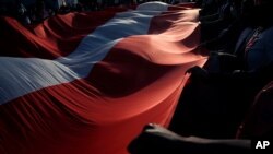 Personas que se niegan a reconocer al nuevo gobierno de Perú sostienen una bandera nacional gigante mientras se reúnen para protestar en la Plaza San Martín, en Lima, el 14 de noviembre de 2021.