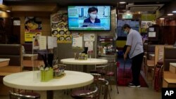 A restaurant employee cleans the floor as a TV screens show Hong Kong Chief Executive Carrie Lam's announcement that the government, invoking an emergency ordinance, will postpone legislative elections, July 31, 2020.