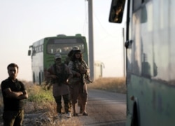 FILE - Rebels from the Hayat Tahrir al-Sham group are seen near buses, outside the villages of al-Foua and Kefraya, Idlib province, Syria, July 18, 2018.