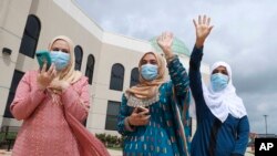 Saba Mahjabeen, right, and Gizman Mawi, center, waive as Sophia Baig looks on during a drive-through Eid al-Fitr celebration outside a closed mosque in Plano, Texas, May 24, 2020. 