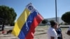 Un partidario sostiene una bandera venezolana con un cartel que se expresa contra el actual presidente de Venezuela, Nicolás Maduro, a la llegada a España del candidato presidencial de la oposición venezolana, Edmundo González Urrutia.