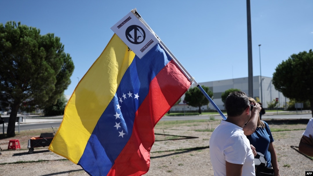 Un partidario sostiene una bandera venezolana con un cartel que se expresa contra el actual presidente de Venezuela, Nicolás Maduro, a la llegada a España del candidato presidencial de la oposición venezolana, Edmundo González Urrutia.
