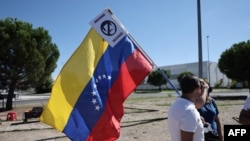 Un partidario sostiene una bandera venezolana con un cartel que se expresa contra el actual presidente de Venezuela, Nicolás Maduro, a la llegada a España del candidato presidencial de la oposición venezolana, Edmundo González Urrutia.