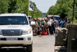 FILE - Cars of the Organization for Security and Cooperation in Europe (OSCE) move as people stand near a checkpoint before crossing the contact line between Russia-backed rebels and Ukrainian troops in Mayorsk, eastern Ukraine, July 3, 2019.