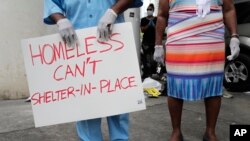 Anthony Swain stands with his wife Connie as he holds a sign advocating for safe housing for the homeless during a news conference by various community organizations, during the new coronavirus pandemic, April 17, 2020, in Miami.