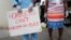 Anthony Swain stands with his wife Connie as he holds a sign advocating for safe housing for the homeless during a news conference by various community organizations, during the new coronavirus pandemic, April 17, 2020, in Miami.