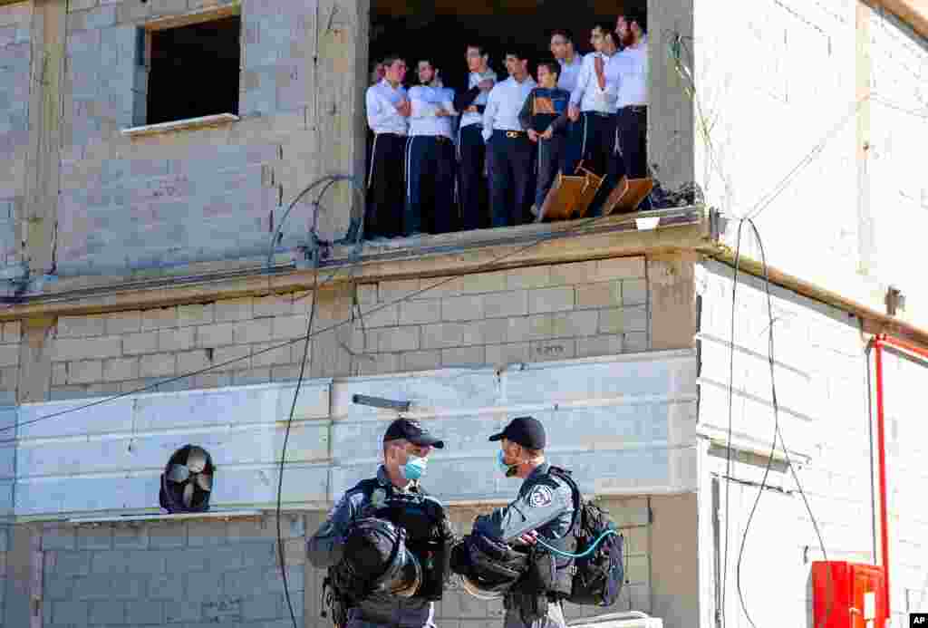 Ultra-Orthodox Jewish seminary students look at Israeli police as they arrive to shutter the Jewish seminary that had opened in violation of coronavirus lockdown rules in Ashdod, Israel. 