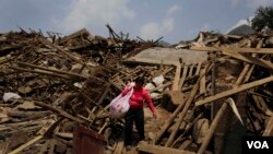 ແມ່ຍິງຄົນນຶ່ງຫີ້ວສິ່ງຂອງຜ່ານຊາກຫັກພັງຂອງເຮືອນຊານ ຫຼັງຈາກເກີດແຜ່ນດິນໄຫວຂະໜາດແຮງ.