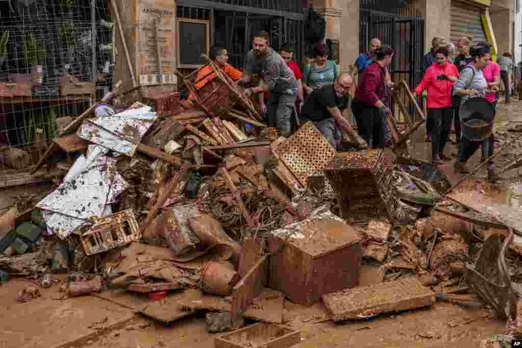 People clean mud from a shop affected by floods in Chiva, Spain.