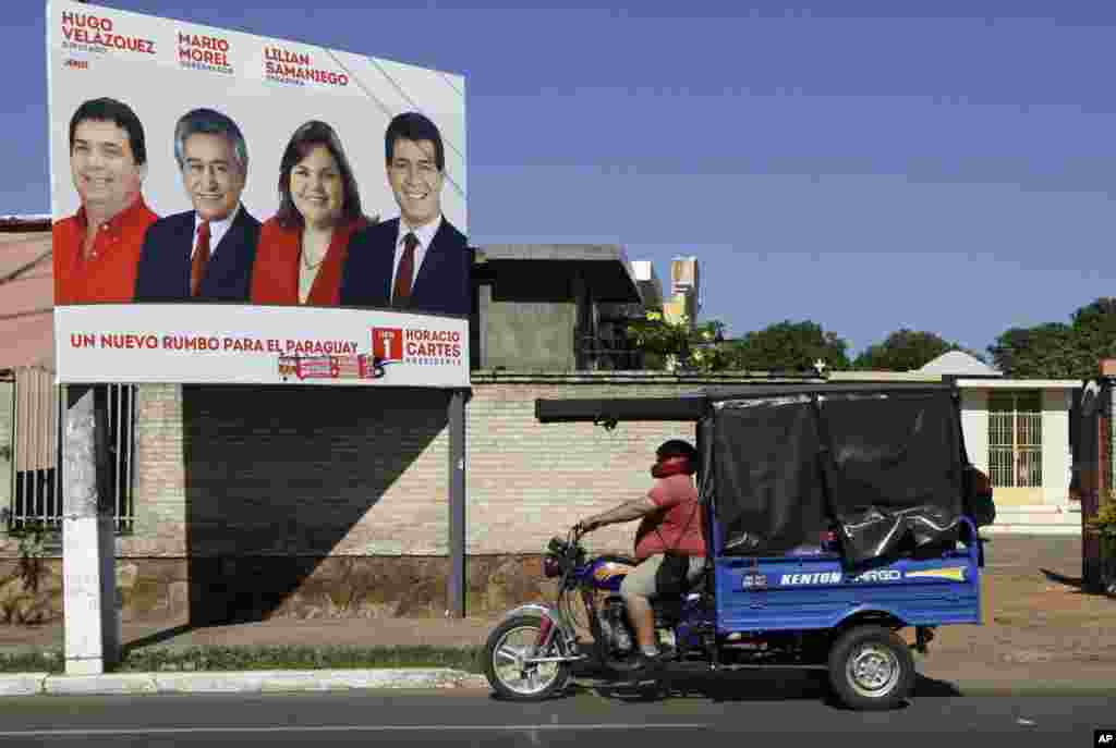 A man drives a motorized tricycle past a billboard picturing Colorado Party's presidential candidate Horacio Cartes, right, in San Lorenzo, Paraguay, April 19, 2013. .