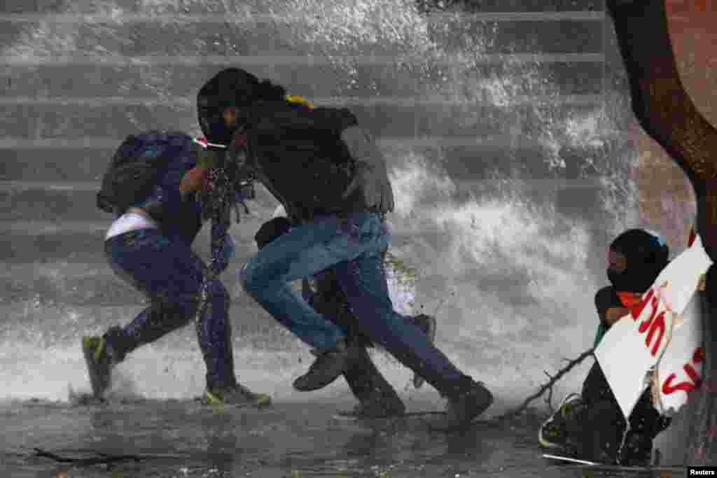 Anti-government protesters run from police water cannon in Caracas, Mar. 20, 2014. Venezuelan intelligence agents arrested one opposition mayor accused of stoking violent protests, while another was jailed for 10 months in the latest moves against rivals of President Nicolas Maduro.