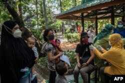 Seorang petugas kesehatan menyuntik seorang wanita dengan dosis vaksin Sinovac Covid-19 saat vaksinasi massal di sebuah kebun binatang di Surabaya pada 13 September 2021. (Foto oleh JUNI KRISWANTO/AFP)