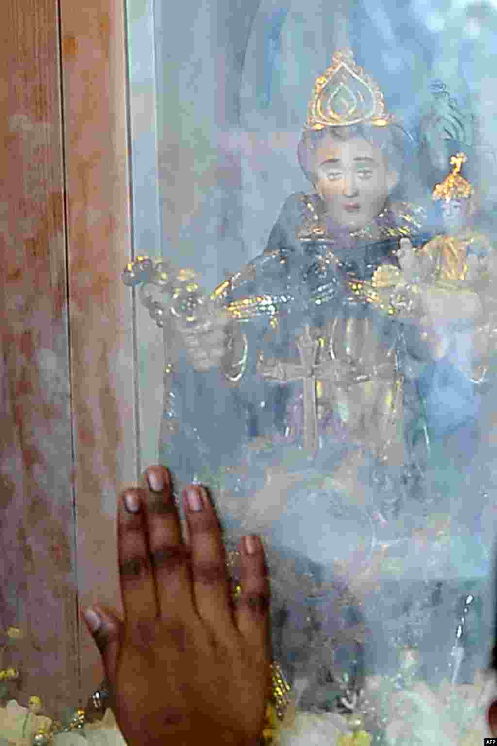 A Sri Lankan Catholic touches the glass near an idol during a mass at a church in Colombo.