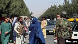 Pasukan Taliban memblokir jalan di sekitar bandara sementara seorang perempuan melintas, di Kabul, Afghanistan, Jumat, 27 Agustus 2021. (Foto: Reuters)