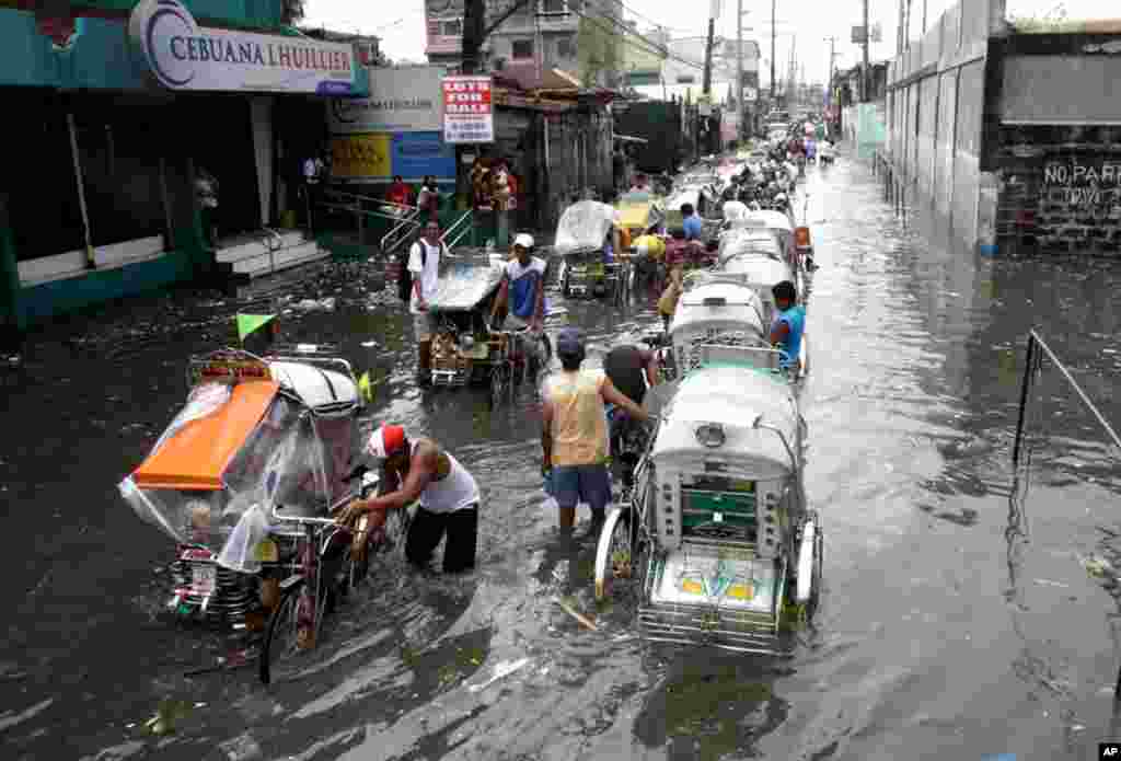 Pedicabs carry passengers through a flooded street as flood waters continue to rise in Navotas City, Philippines, Aug. 2, 2012.