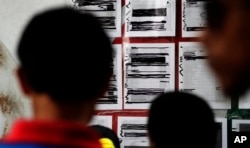 FILE - Migrants seeking asylum in the United States check their names on a printed list that's posted on a board near the international bridge, April 30, 2019, in Matamoros, Mexico.