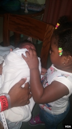 Agnes' daughter holds her baby brother, born in a Washington, D.C. hospital, for the first time. (J.Oni/VOA)
