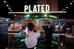 Seorang pelanggan mengambil pesanannya dari food truck hamburger di Al Aali Mall, di Manama, Bahrain, di tengah pandemi COVID-19, 27 Februari 2021. (REUTERS/Hamad I Mohammed)