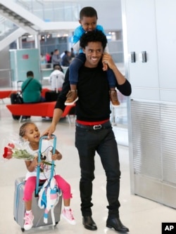 Olympic silver medalist Feyisa Lilesa, of Ethiopia, carries his son Sora, 3, and pulls along his daughter Soko, 5, after picking up his family at Miami International Airport, Feb. 14, 2017.