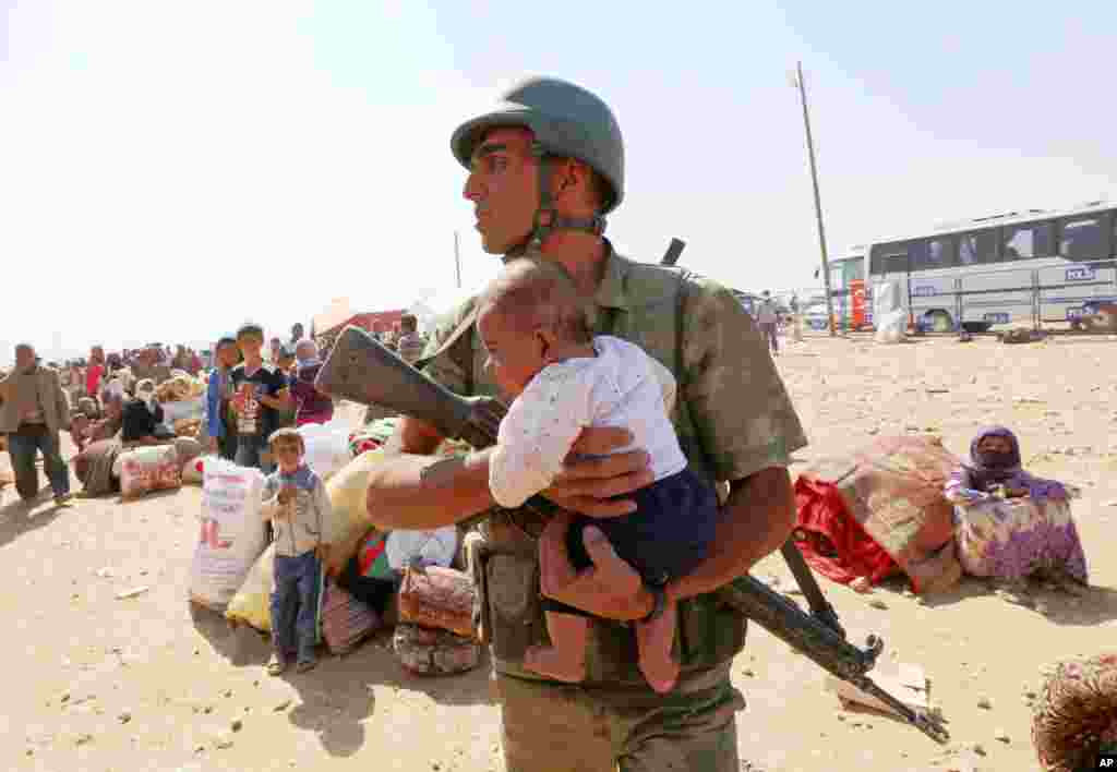 Seorang tentara Turki menggendong bayi yang terpisah dengan ibunya saat pengungsi Kurdi-Suriah dari&nbsp;Kobani memasuki kita Suruc, Turki. 