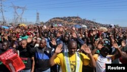 Miners gesture as they pray during the one-year anniversary commemorations to mark the killings of 34 striking platinum miners fatally shot by police outside the Lonmin's Marikana platinum mine in Rustenburg, 100 kilometers northwest of Johannesburg, Aug.