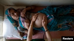 Suman, a 25-year-old pregnant woman, lies on an examination table as a nurse places her hands on her stomach during a check up at a community health centre in the remote village of Chharchh, in the central Indian state of Madhya Pradesh.