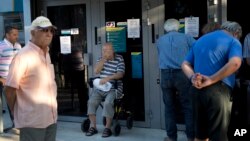 Pensioners wait outside a national bank branch to withdraw a maximum of 120 euros for the week in central Athens, Monday, July 13