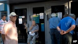 Pensioners wait outside a national bank branch to withdraw a maximum of 120 euros for the week in central Athens, Monday, July 13