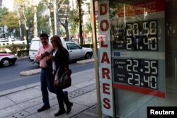 People walk pass a board displaying the exchange rate of Mexican peso against the U.S. dollar in Mexico City, Jan. 11, 2017.