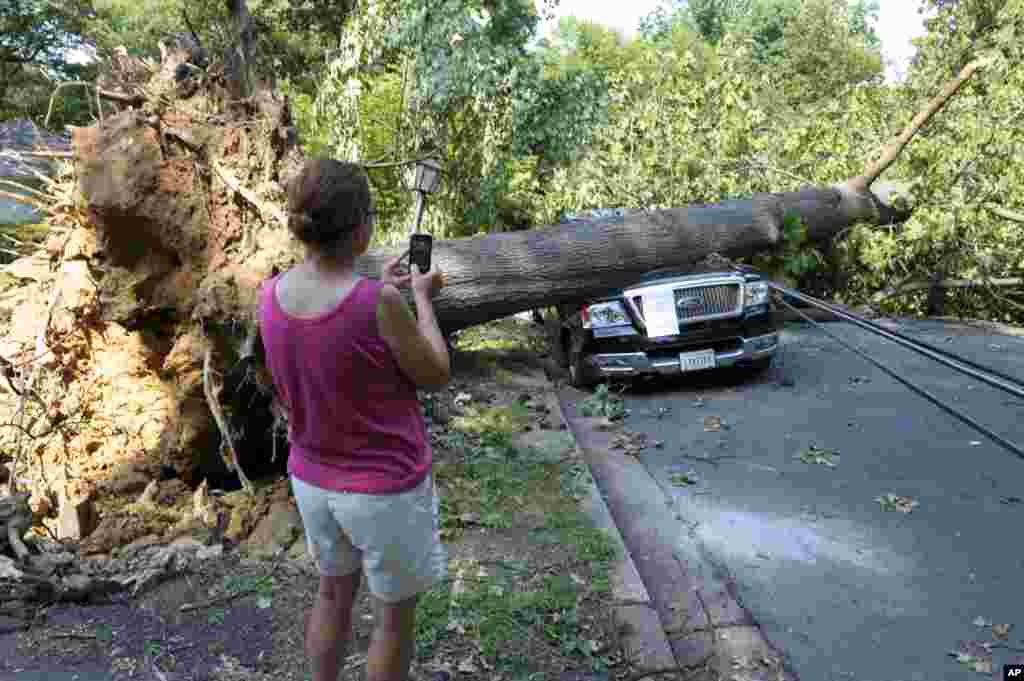 A woman takes photograph of Mike Wolfe's pick-up truck as it lies under a fallen tree in front of his house after a severe storm in Falls Church, Va., June 30, 2012.