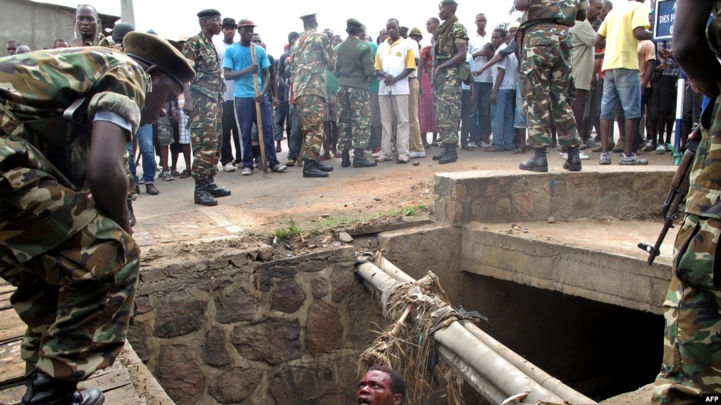 FILE - A man begs for help from the military as he stands in a drain where he had hidden to escape a lynch mob at the Cibitoke district of Burundi's capital, Bujumbura. International judges have approved the opening of a full investigation into alleged crimes against humanity in Burundi, where at least 1,200 people have died in unrest since 2015.