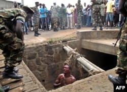FILE - A man begs for help from the military as he stands in a drain where he had hidden to escape a lynch mob at the Cibitoke district of Burundi's capital, Bujumbura.