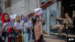 A Taliban fighter watches as Afghan women hold placards during a demonstration demanding better rights for women in front of the former Ministry of Women Affairs in Kabul on September 19, 2021.