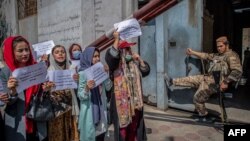 Një luftëtar taleban vështron, ndërsa gratë mbajnë pankarta gjatë një demonstrate përpara ish-Ministrisë së Çështjeve të Grave në Kabul (19 shtator 2021)