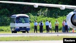 FILE - Asylum seekers are pictured being transported from an aircraft to a bus on the island of Nauru. A Somali refugee who alleged she was raped in Nauru will be flown to Australia for a second time to potentially have an abortion.