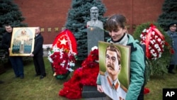 A woman holds a portrait of Joseph Stalin near the former Soviet leader's tomb near the Kremlin wall, as she came to mark the 136th anniversary of his birth, in Moscow, Russia, Dec. 21, 2015. 