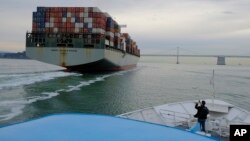 FILE- In this March 7, 2018, file photo, a man standing on the bow of a Golden Gate Ferry takes a picture of a container ship as it heads toward the San Francisco-Oakland Bay Bridge in San Francisco.