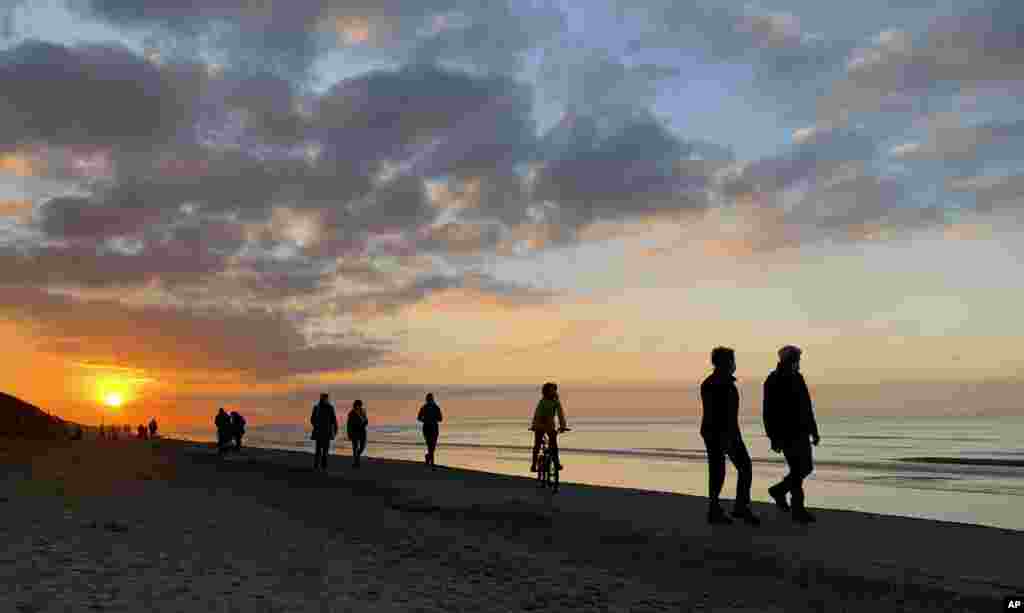 The sun begins to set as people walk along the seaside in Adinkerke, Belgium, Thursday, Nov. 5, 2020. Seaside towns in Belgium were busier than usual due to coronavirus, COVID-19 restrictions and school holiday. (AP Photo/Virginia Mayo)
