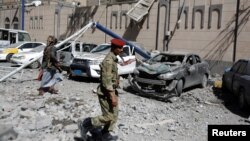 Houthi militants walk past damaged cars outside the Presidential Compound after it was hit by air strikes in Sanaa, Yemen, May 7, 2018. 