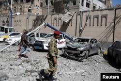 FILE - Houthi militants walk past damaged cars outside the Presidential Compound after it was hit by air strikes in Sana'a, Yemen, May 7, 2018.