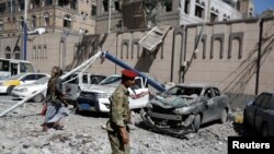 Para militan Houthi berjalan melewati mobil-mobil yang rusak di luar komplek kepresidenan setelah serangan udara di Sanaa, Yaman, 7 Mei 2018. 