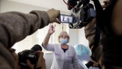 A Russian medical worker, center, shows a vial with Russia's Sputnik V coronavirus vaccine to the media prior to a shot in a hospital in Vladivostok, Russia, on Tuesday, Dec. 15, 2020. (AP Photo/Aleksander Khitrov )